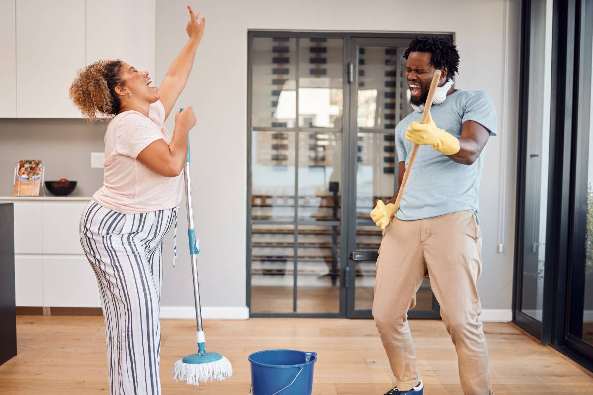 Shot of a young couple singing and dancing while cleaning at home.